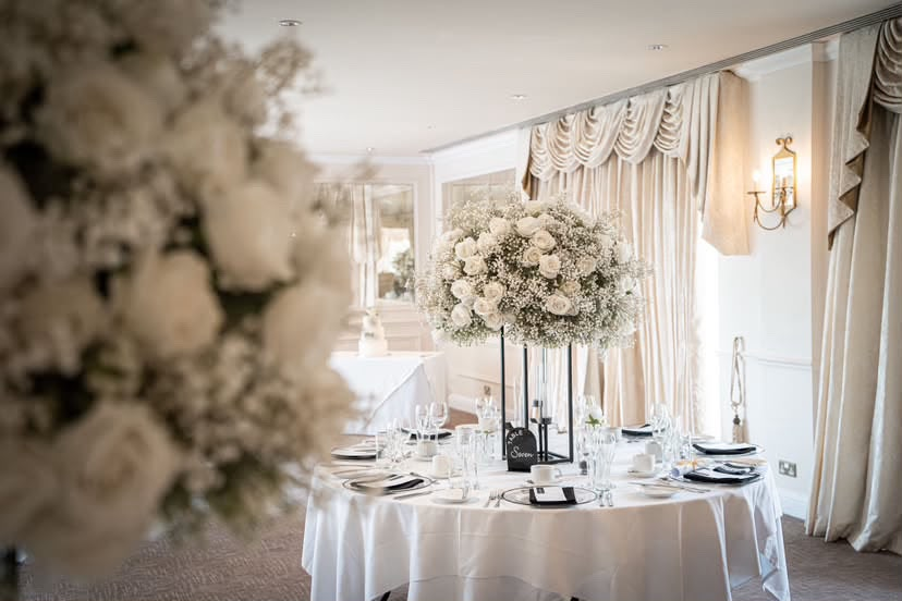 Sophie and Tom's wedding breakfast table with a tall white rose centrepiece and a Table Seven sign, styled by Laye's