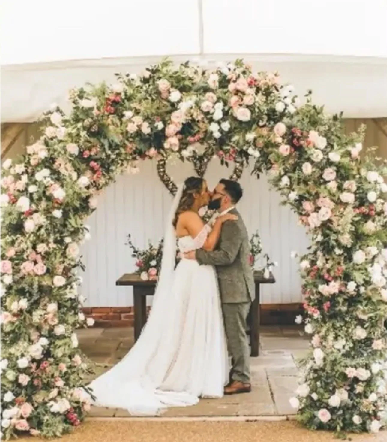 Couple kissing beneath a blush floral arch styled by Laye's